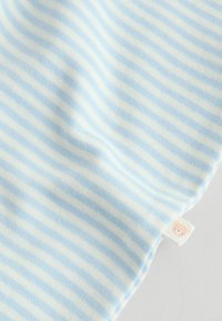 Svetlomodrá a bielo pruhovaná tkanina s jemnou textúrou. V spodnom rohu je malý štítok s medvedíkovou tvárou.