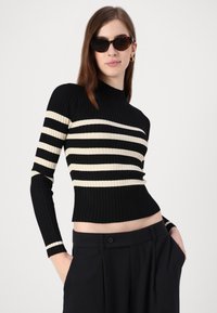 Μαύρος και κρεμ ριγέ πλεκτός πουλόβερ με υψηλή λαιμόκοψη και μακριά μανίκια, με διακοσμητικές ρίγες και κοντή εφαρμογή.