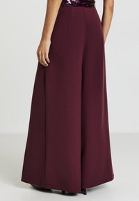 Pantaloni a gamba larga in tessuto bordeaux, con una texture liscia e una vestibilità sartoriale. Nessuna ferramenta o motivo visibile.