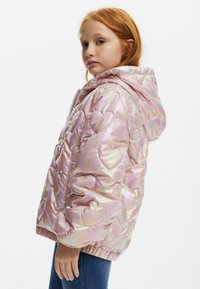 Iridescent rosa pufferjacka med huva, hjärtformad kviltad mönster, elastiska muddar och fåll. Bärs över blå jeans, inget synligt hårdvara.