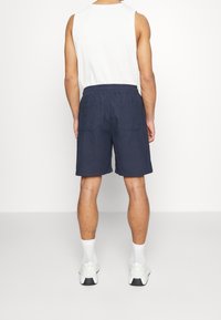 Pantalones cortos azul marino con cinturilla elástica, que cuentan con dos bolsillos traseros, combinados con una camiseta sin mangas blanca y zapatillas deportivas blancas.