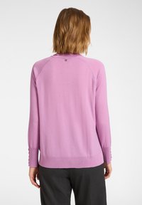 Jasnoróżowy dzianinowy sweter z długimi rękawami, ściągaczami na mankietach i małym logo przy dekolcie. Miękka faktura i luźny krój.