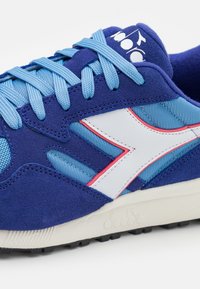 Blue suede and mesh sneakers feature a white leather logo, contrasting pink accents, and textured rubber sole with black tread.