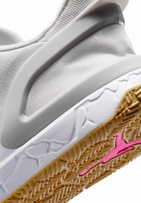 Witte atletische schoenhak met een gestructureerde witte tussenzool met het Jumpman-logo in reliëf, een buitenzool van rubber in karamelkleur en een zichtbaar roze Jumpman-logo op de zool.