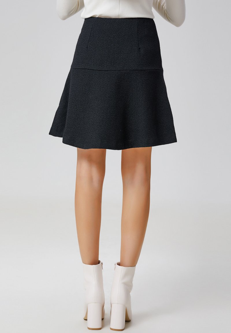 Jupe noire évasée en tissu texturé avec une taille lisse et des poches latérales ; associée à des bottines blanches à talons carrés.