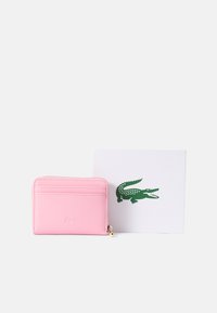 Pink leather card holder with multiple slots and zipper; features embossed logo. Accompanied by a white card with a green crocodile graphic.