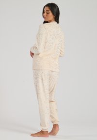 Set di abbigliamento comodo in un beige chiaro con una texture morbida; presenta un motivo a pois dorati. La giacca ha maniche lunghe, i pantaloni hanno polsini elastici.