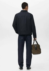 Chaqueta de mezclilla azul marino con cuello, jeans negros y llevando un bolso verde oliva con acentos negros. Textura suave y diseño estructurado.
