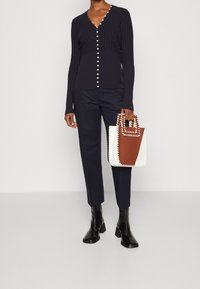 Cardigan a coste blu con bottoni in perla, abbinato a pantaloni blu sartoriali e stivali neri con tacco. Include una borsa strutturata bicolore.
