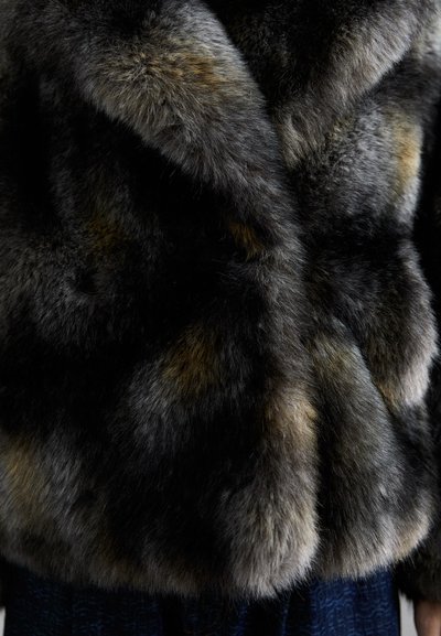 Zbliżenie na ciemnobrązowy i szaro-futrzany płaszcz noszony na ciemnoniebieskim wzorzystym materiale.