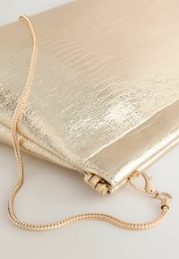 Goldfarbene Metallic-Clutch mit texturierter Oberfläche, ausgestattet mit einer Kettenriemen und einem Verschluss. Schlanke, kantige Form, kompaktes Design.