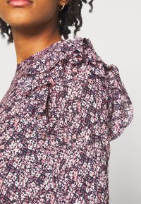 Bluse mit Blumenmuster und Rüschendetails an den Schultern; überwiegend dunkelblau mit pinken und weißen Akzenten; leichtes Gewebe.