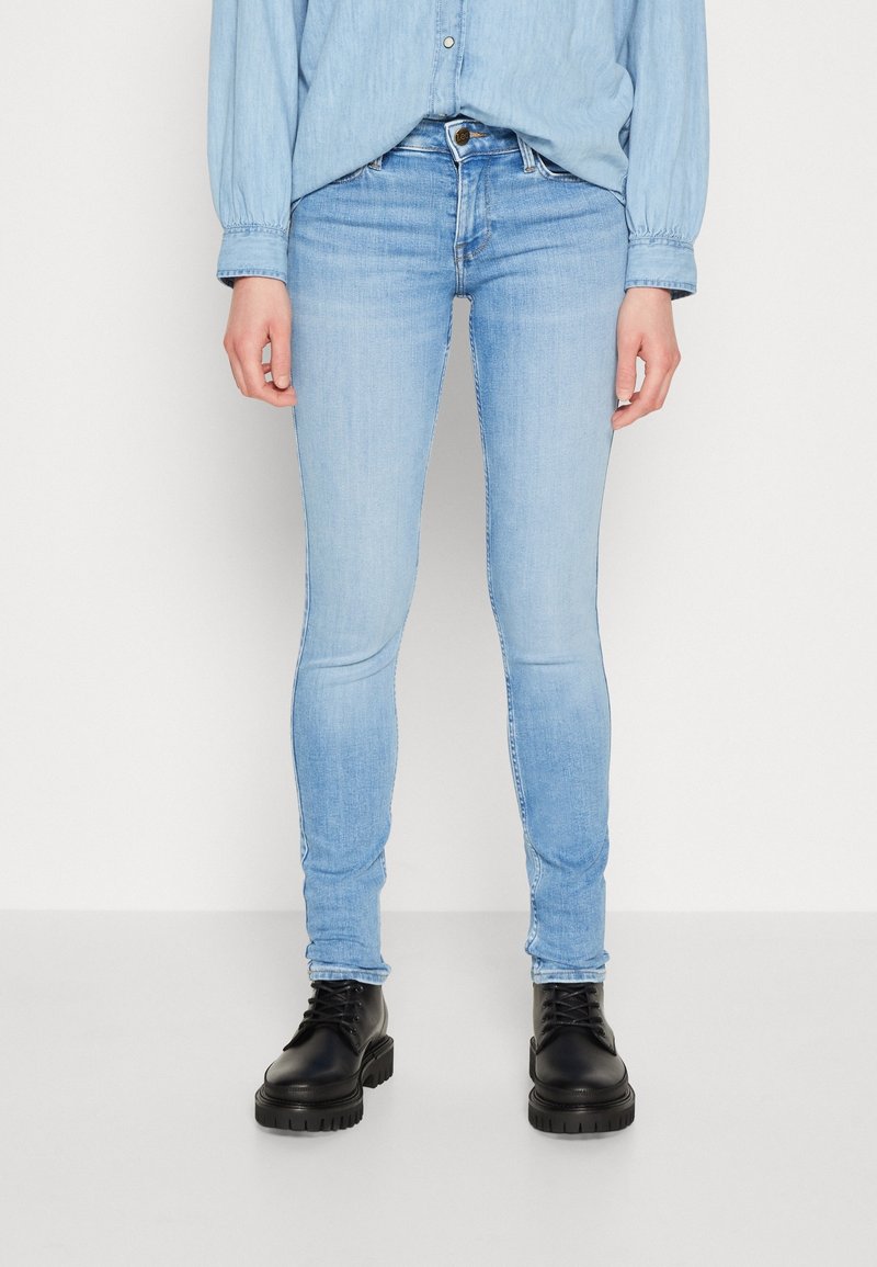 Jeans ajustados de color azul claro con un lavado desteñido, cintura de media altura y costuras mínimas. Combinados con botas negras con cordones.