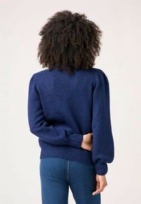 Pull bleu foncé avec manches bouffantes, poignets et ourlet côtelés. Texture douce et motif chiné subtil, associé à un jean ajusté.