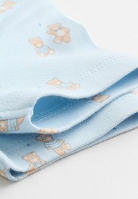 Helehelesinine kangas, millel on pruuni ja heleda pruuni värvi karu muster, pehme tekstuur ja õmmeldud servad, näidates volditud äärte detaile.