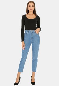 Czarny body z długim rękawem w połączeniu z jasnoniebieskimi, wysokimi spodniami typu straight-leg. Całość dopełniają szpilki.