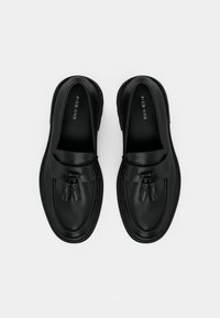 Black leather loafers with a rounded toe and a tassel accent. Smooth texture and a contrasting stitched sole. Brand name inside.