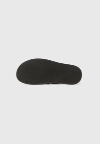 Semelle de chaussure en caoutchouc noir avec un motif en chevrons texturé et des bords arrondis, conçue pour l'adhérence et la durabilité.