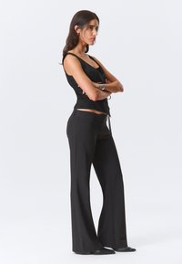 Débardeur noir ajusté avec larges bretelles, associé à un pantalon noir évasé taille haute. Les deux vêtements ont une texture lisse et une coupe slim.