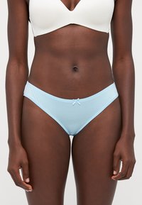 Slip bikini in cotone azzurro chiaro, caratterizzato da una texture morbida, un taglio a vita bassa e un piccolo fiocco decorativo sul davanti. Design semplice e minimale.