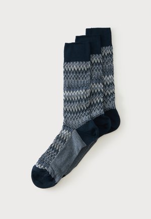 Drie paar sokken tot halverwege de kuit met donkerblauwe tenen, hielen en boorden en een zigzag gebreid patroon in blauw, wit en grijstinten.