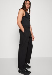 Crna majica bez rukava s prilagodenim dizajnom, uparena s krojenim crnim hlačama i debelim crnim tenisicama. Glatka tekstura kroz cijeli outfit.