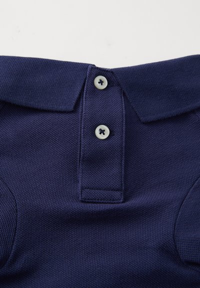 Marineblå polo skjorte med teksturert stoff, tre knapper, og klassisk krage. Knapper er lyse med mørk tråddetalj.