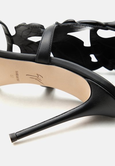 Μαύρο πέδιλο με ψηλό τακούνι, λεπτό λουράκι, σχέδιο με κομμένα λουλούδια, μυτερό τακούνι και μπεζ σόλα με ενδείξεις μεγέθους και προέλευσης.