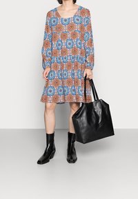 Vestido de estampado floral en azul, naranja y blanco; mangas largas, cuello redondo. Un bolso de cuero negro y botas de tobillo completan el look.