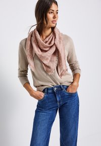 Ljusrosa halsduk med ett subtilt mönster och fransade kanter, bärs över en beige tröja och blå jeans. Mjukt tyg som hänger löst.