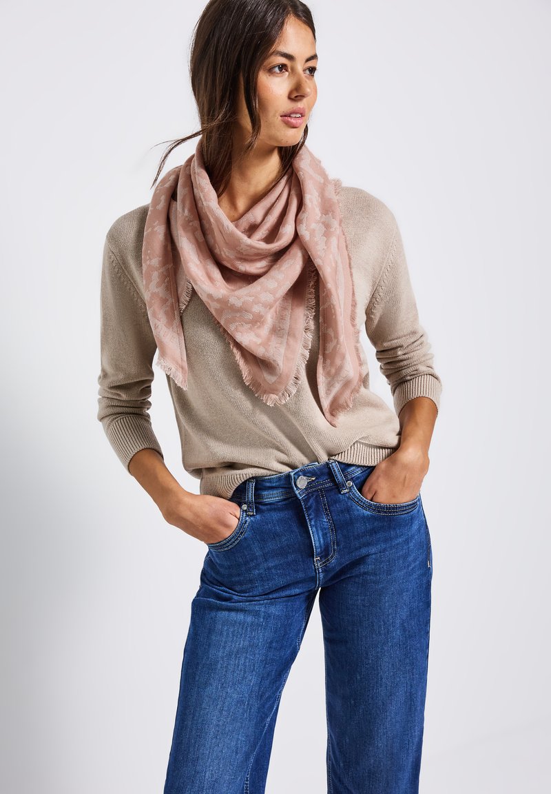 Ljusrosa halsduk med ett subtilt mönster och fransade kanter, bärs över en beige tröja och blå jeans. Mjukt tyg som hänger löst.