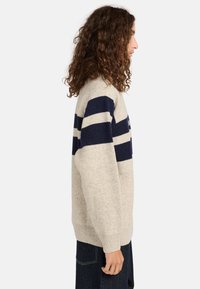 Beżowy sweter z granatowymi poziomymi paskami, wykonany z miękkiego dzianiny. Posiada okrągły dekolt i ribbowane mankiety, zaprojektowany dla luźnego kroju.