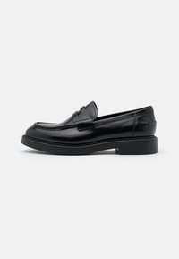 Mocassins en cuir verni noir avec un bout arrondi, des détails de couture surélevés et une semelle noire basse et solide. Avec un accent de sangle à l'avant.