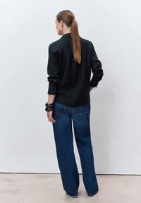 Black button-up shirt with long sleeves, paired with high-waisted, wide-leg blue denim jeans, viewed from the back.