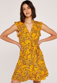 Gelbes Paisley-Musterkleid mit Rüschensäumen, tiefem V-Ausschnitt und Bindegürtel in der Taille. Leichter Stoff mit ausgestellt geschnittenem Saum.