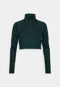 Přiléhavý crop top pulovr z tmavě zelené tkaniny, s vysokým límcem a čtvrtinovým zipem, dlouhými raglánovými rukávy a přizpůsobeným střihem.