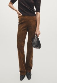 Brown suede flared pants, smooth texture, high waist; paired with a black leather bag. Black pointy-toed shoes complete the outfit.