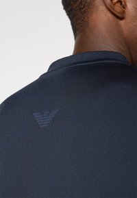 Polo azul-escuro com mangas curtas, apresentando um tecido texturizado e um discreto logotipo em relevo na parte de trás do colarinho.