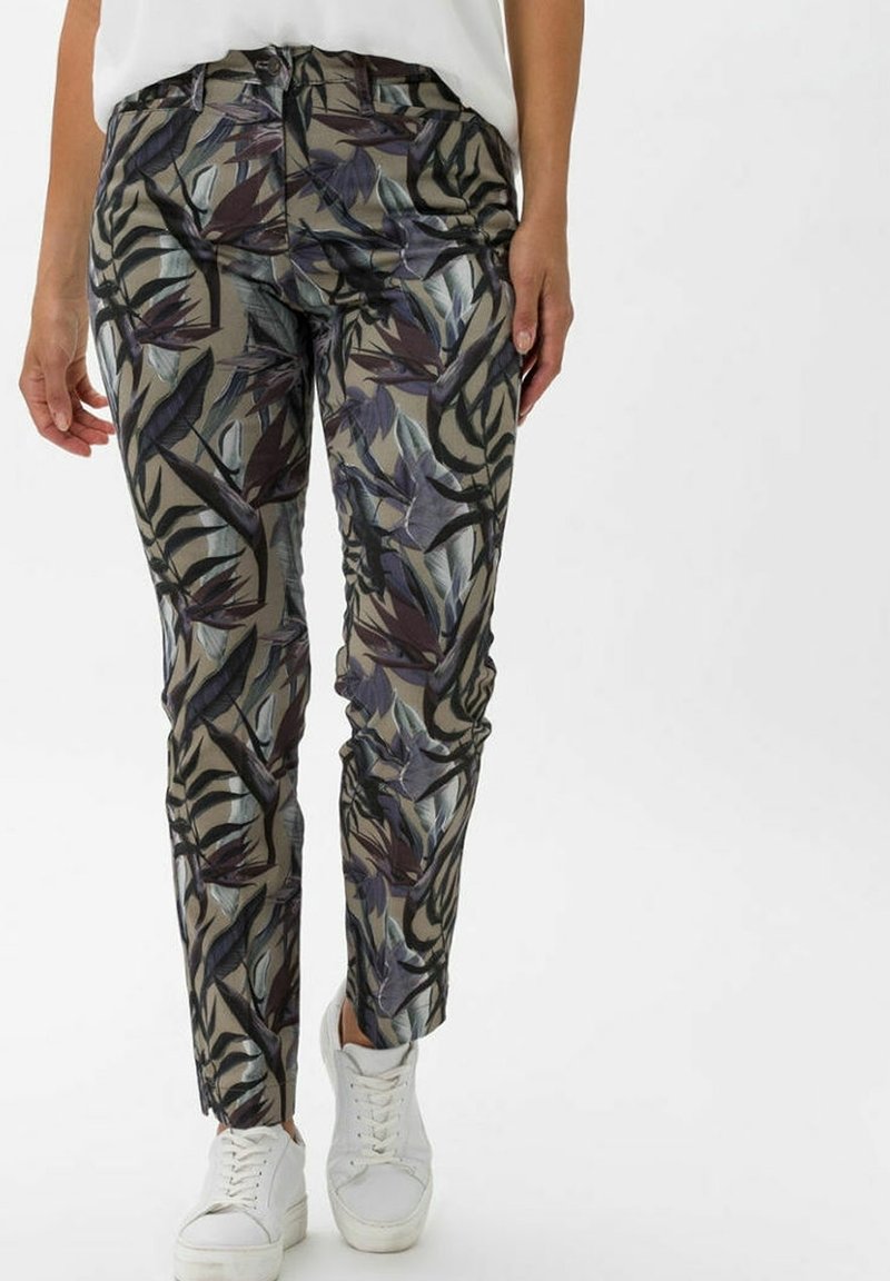Pantalon slim avec motifs de feuilles vert foncé et violettes, associé à des baskets blanches et un haut blanc sur un fond uni.