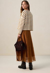 Striped long-sleeve top in cream and brown, paired with a brown lace maxi skirt. Accessories include a dark burgundy handbag with eyelet details and boots.