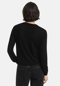 Zwarte gebreide trui met lange mouwen, ronde hals en een licht losse pasvorm, gecombineerd met donkergrijze jeans, gezien van de achterkant.