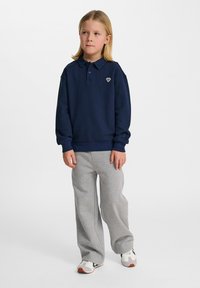 Mörkblå långärmad polo med knäppbar krage och liten broderad design, matchad med grå mjukisbyxor och vita sneakers.