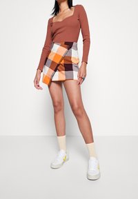 Brunrandig långärmad topp som matchas med en flerfärgad rutad minikjol i orange, vitt, brunt och grått. Vita sneakers med gula accenter.