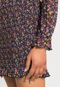 Vestido curto preto com padrão floral, com bainha e mangas com volante. Apresenta uma textura franzida e um padrão floral multicolorido por todo o vestido.