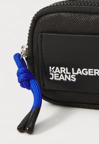 Svart nylonfodral med dragkedja och strukturerad yta, med en blå dragremsa och en framträdande vit logotyp som säger "KARL LAGERFELD JEANS."