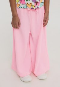 Pantaloni a gamba larga rosa chiaro realizzati in tessuto testurizzato con vita regolabile con cordoncino. Abbinati a sneakers bianche.
