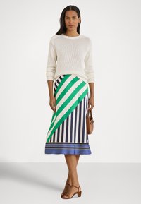 Casaco branco de malha, saia com riscas diagonais verdes e brancas com riscas verticais azul-marinho e creme, mala castanha de ombro, sandálias castanhas.