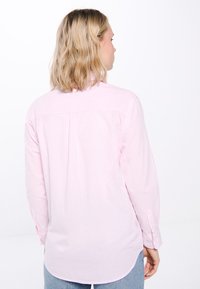 Long-sleeve shirt in light pink with white stripes, featuring a button-down collar and a curved hem, made from a smooth fabric.