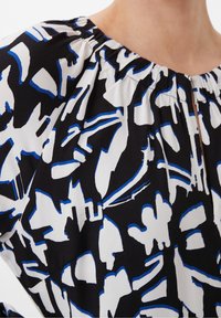 Tela negra con un atrevido patrón abstracto en blanco y azul, con un escote fruncido y un ajuste relajado. Textura suave.