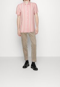 Kortärmad rosa randig skjorta med vita linjer, beige manchesterbyxor och svarta skor. Slät tyg och normal passform.